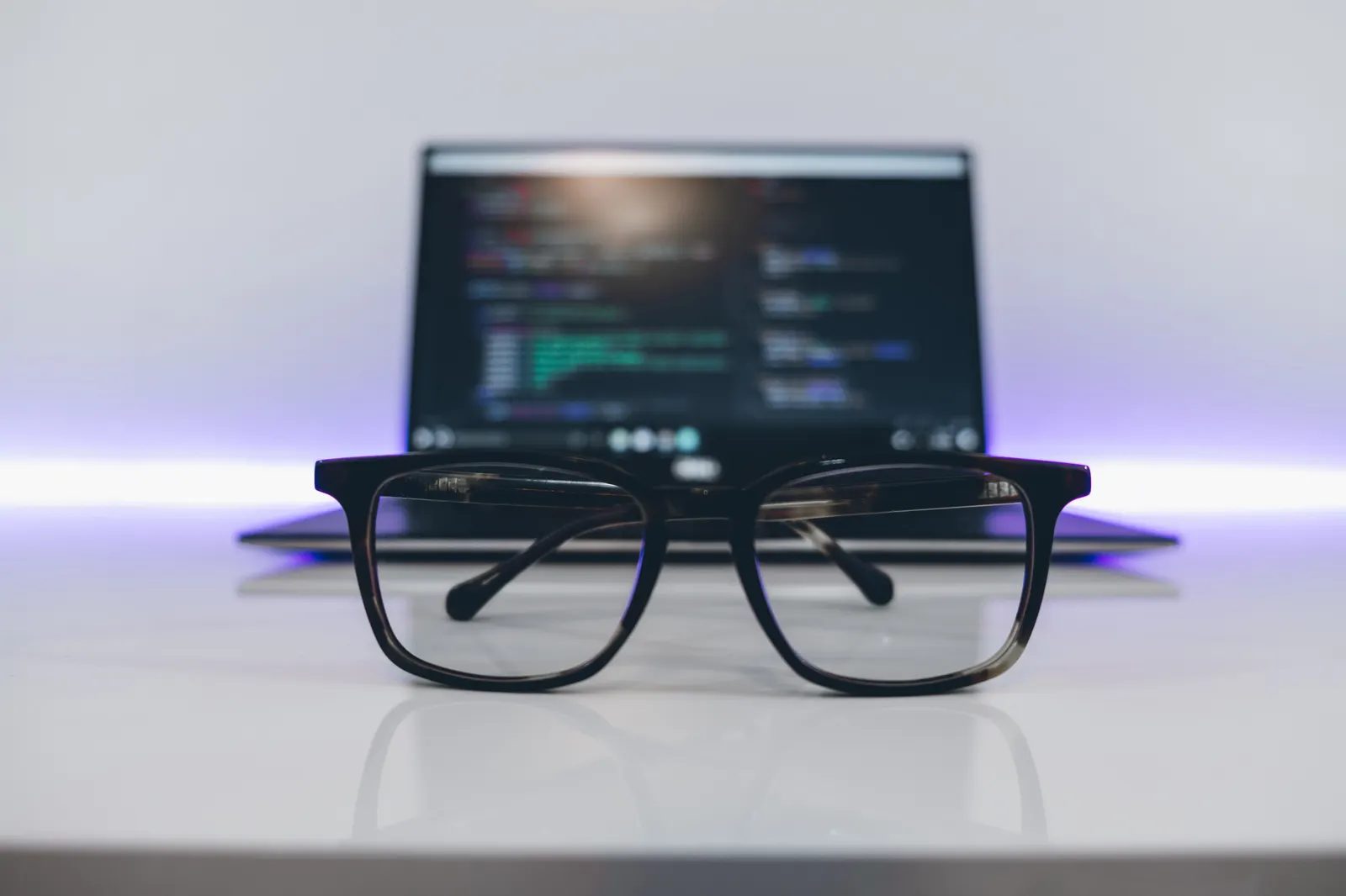 Laptop on a desk with a pair of glasses in front of the screen